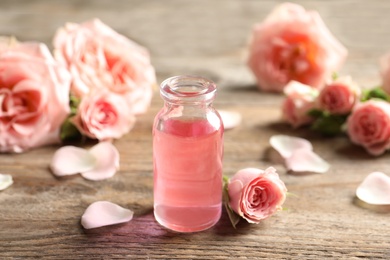 Photo of Bottle of rose essential oil and flowers on wooden table