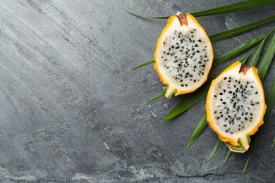Photo of Delicious cut dragon fruit (pitahaya) and tropical leaf on grey table, flat lay. Space for text