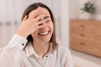 Photo of Beautiful woman covering eyes while laughing in room, space for text