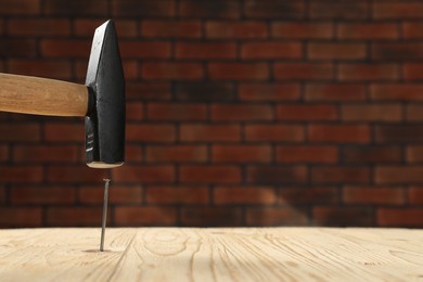 Hammering metal nail on wooden table against brick wall. Space for text