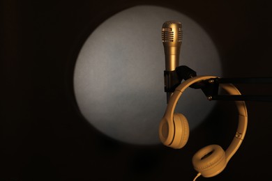 Stand with microphone and headphones in spotlight on black background, space for text. Sound recording and reinforcement