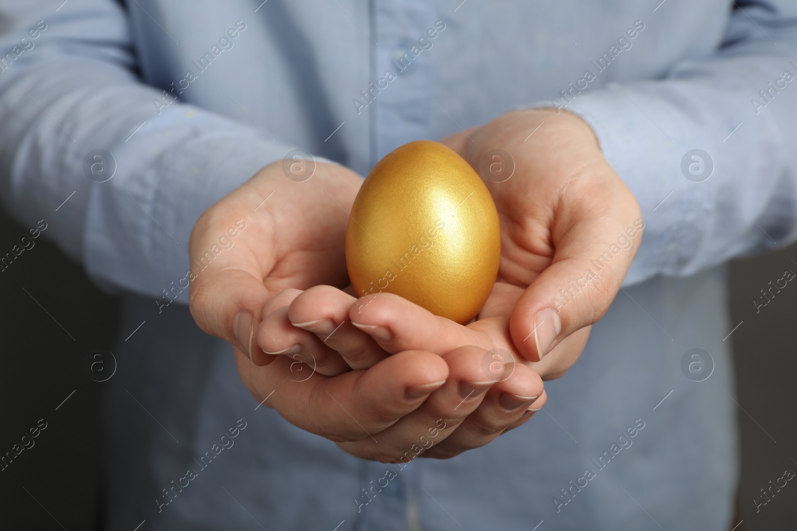 Photo of Woman holding shiny golden egg on grey background, closeup