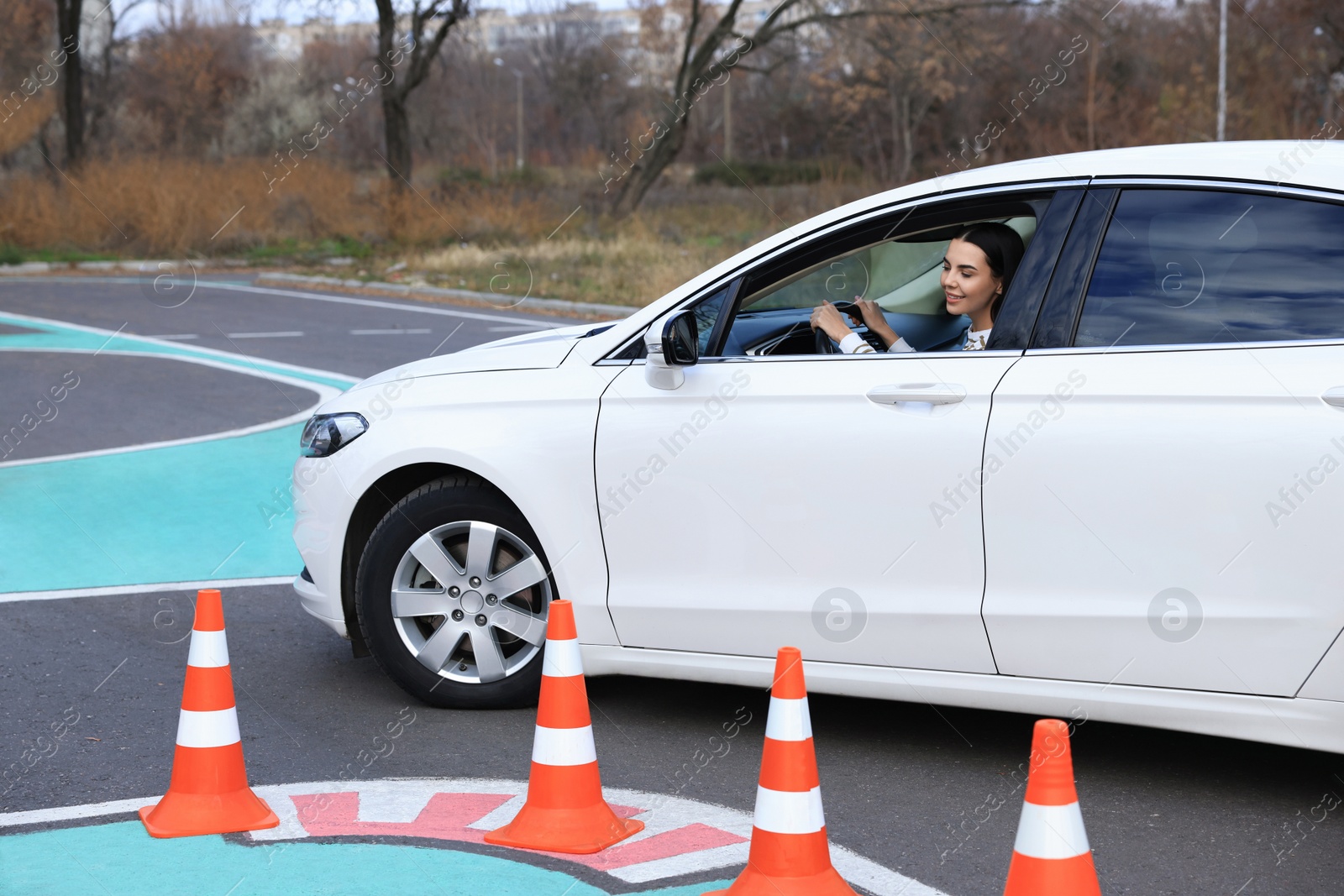 Photo of Young woman in car on test track with traffic cones. Driving school