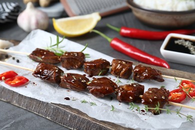 Skewers with pieces of tasty chicken meat glazed in soy sauce and other products on grey table, closeup