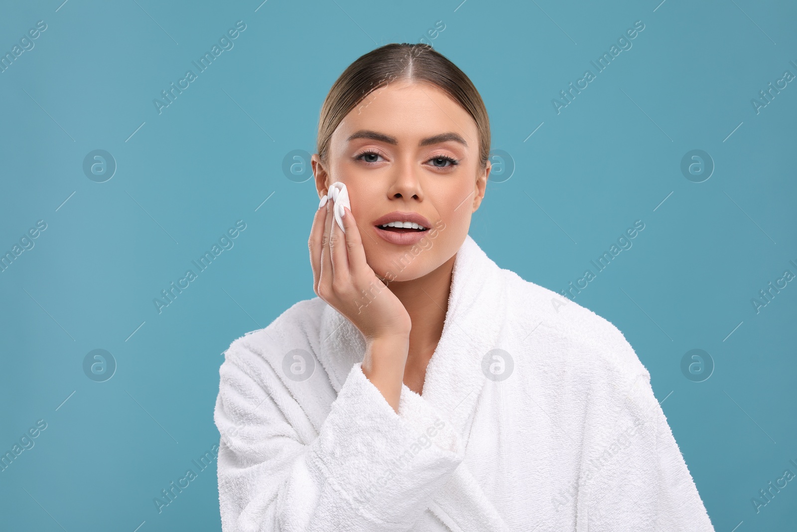 Photo of Beautiful woman removing makeup with cotton pad on light blue background