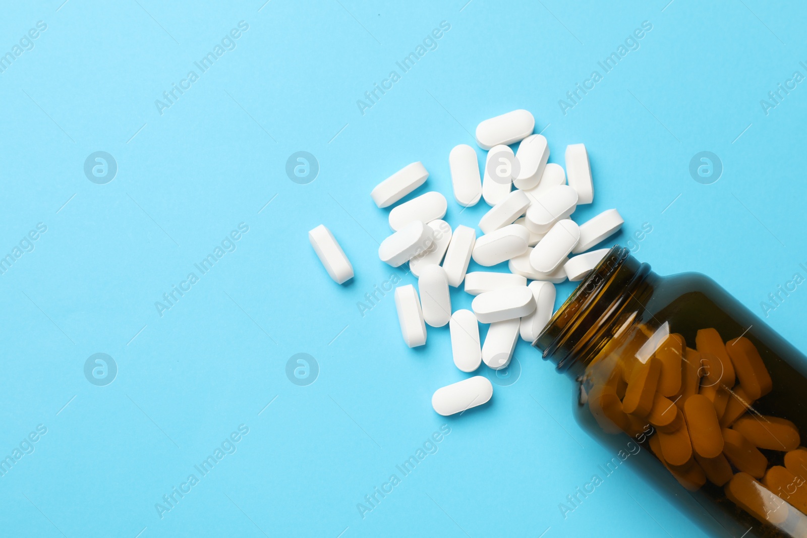 Photo of Bottle and vitamin capsules on light blue background, top view. Space for text