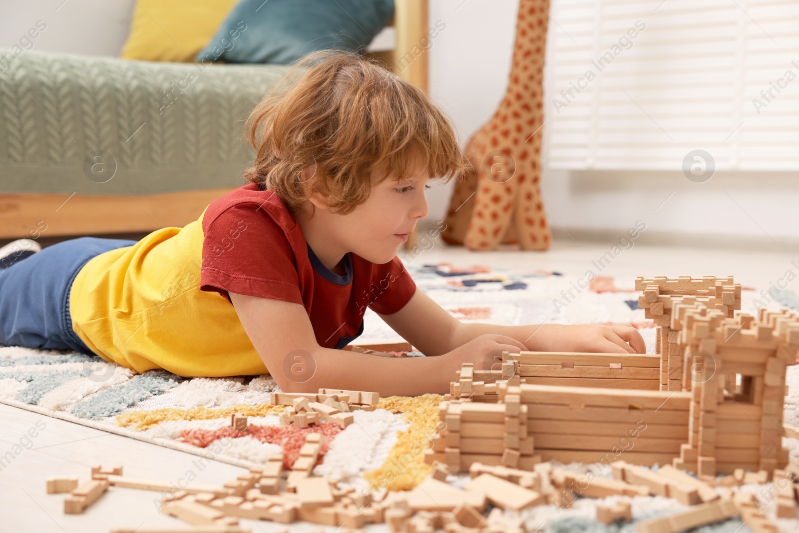 Photo of Little boy playing with wooden construction set on carpet in room. Child's toy