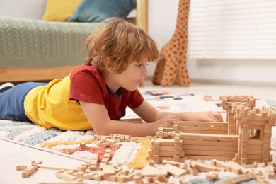 Little boy playing with wooden construction set on carpet in room. Child's toy