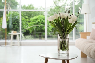 Photo of Beautiful bouquet of willow branches and tulips in vase on table indoors, space for text
