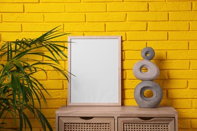 Photo of Empty frame and decor on wooden cabinet near yellow brick wall. Mockup for design