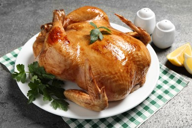 Photo of Tasty roasted chicken with parsley and lemon on grey textured table