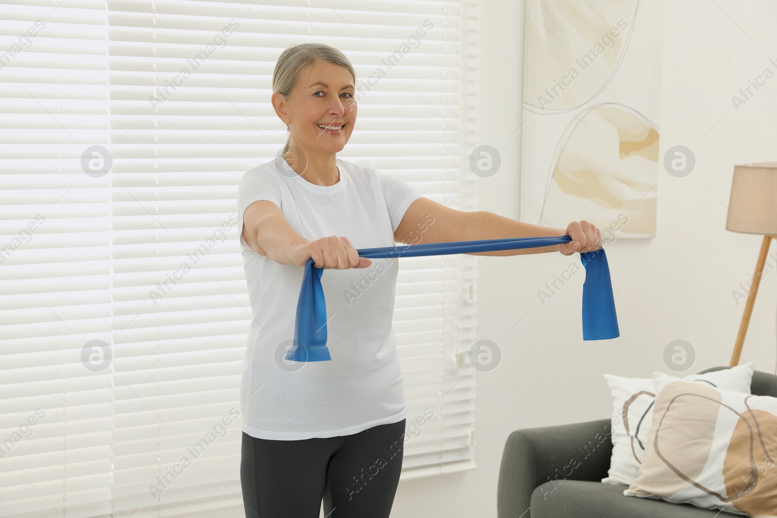 Photo of Senior woman doing exercise with fitness elastic band at home