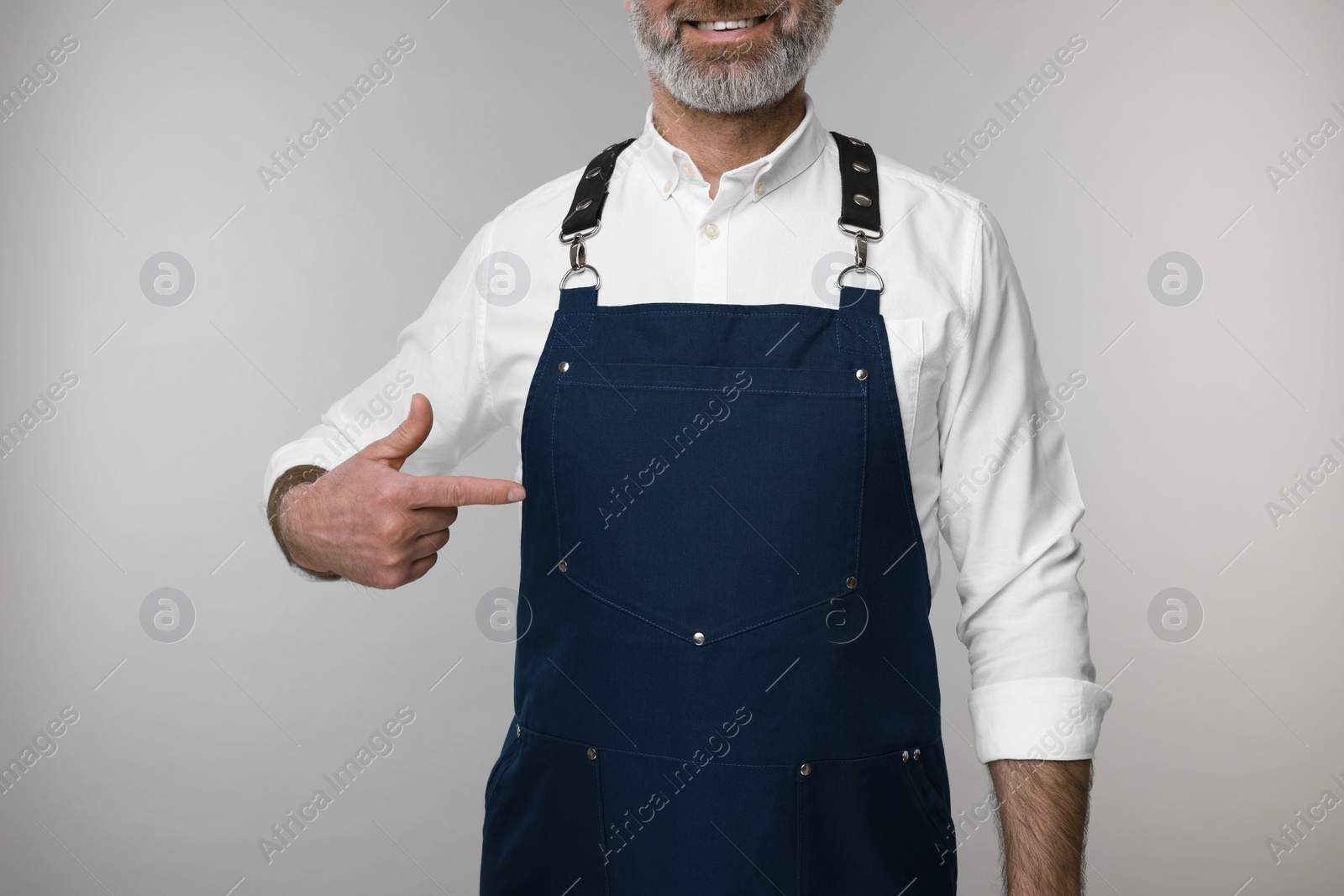 Photo of Man pointing at kitchen apron on grey background, closeup. Mockup for design