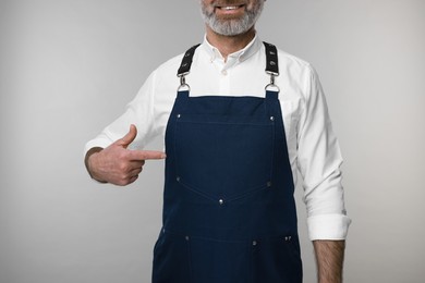 Photo of Man pointing at kitchen apron on grey background, closeup. Mockup for design