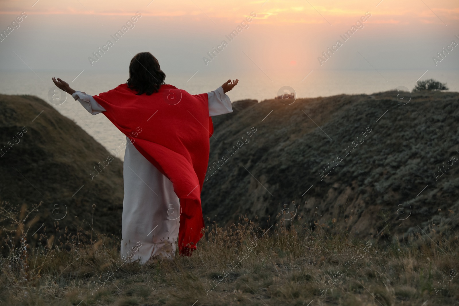 Photo of Jesus Christ raising hands on hills at sunset, back view. Space for text