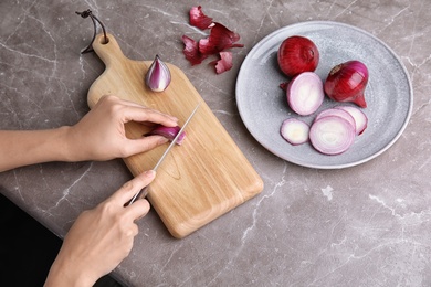 Woman cutting ripe red onion on table