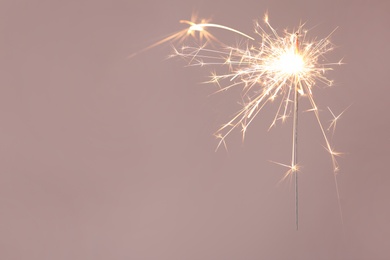 Photo of Bright burning sparkler on beige background, closeup. Space for text