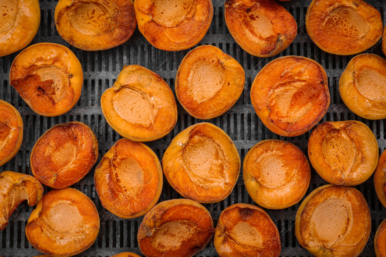 Photo of Many halved apricots on metal drying rack, flat lay