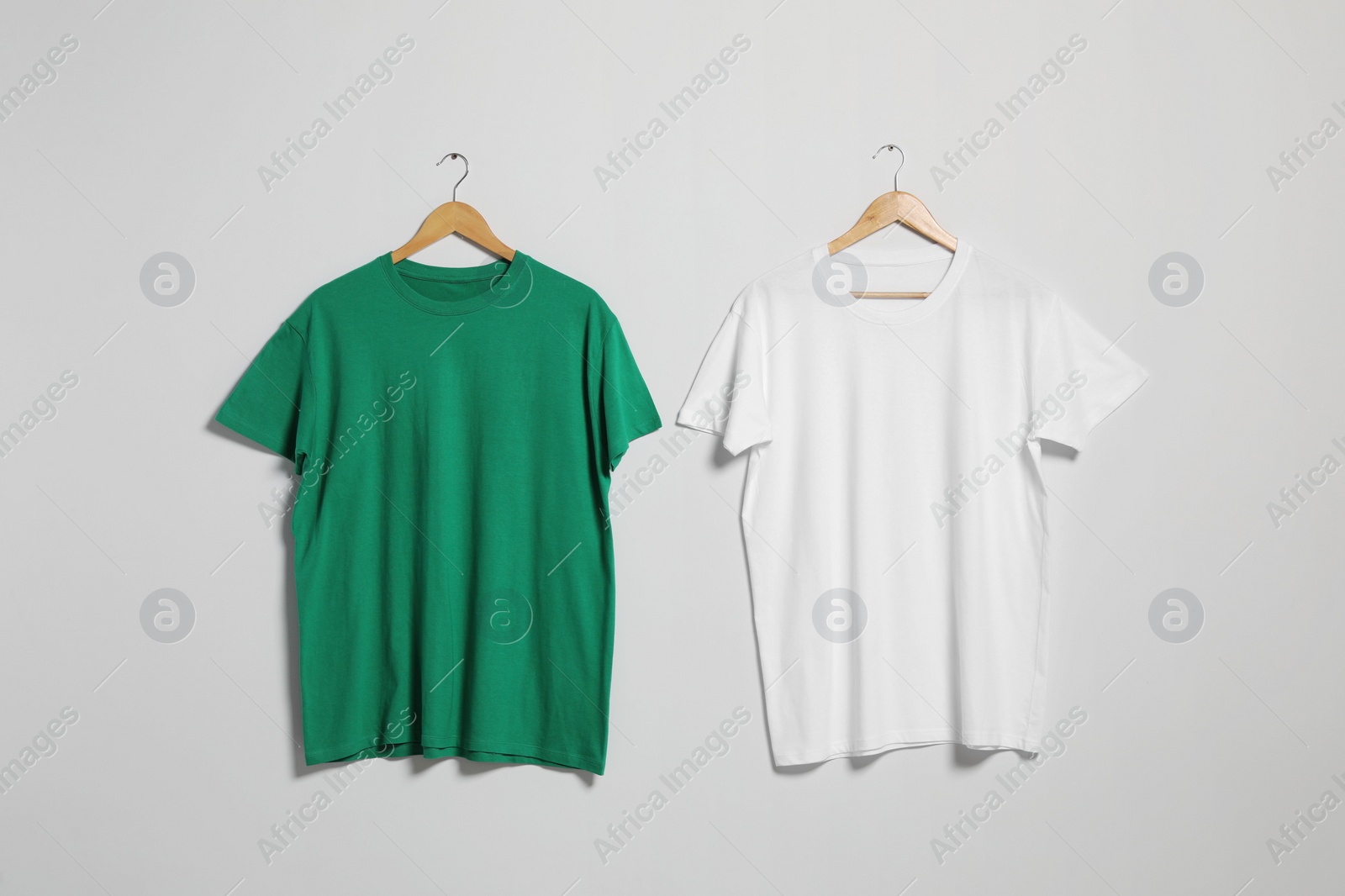 Photo of Hangers with different t-shirts on light wall. Mockup for design