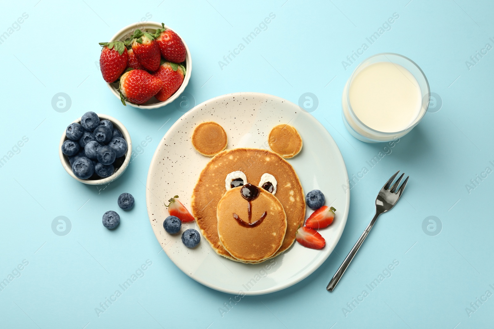 Photo of Creative serving for kids. Plate with cute bear made of pancakes and berries on light blue table, flat lay