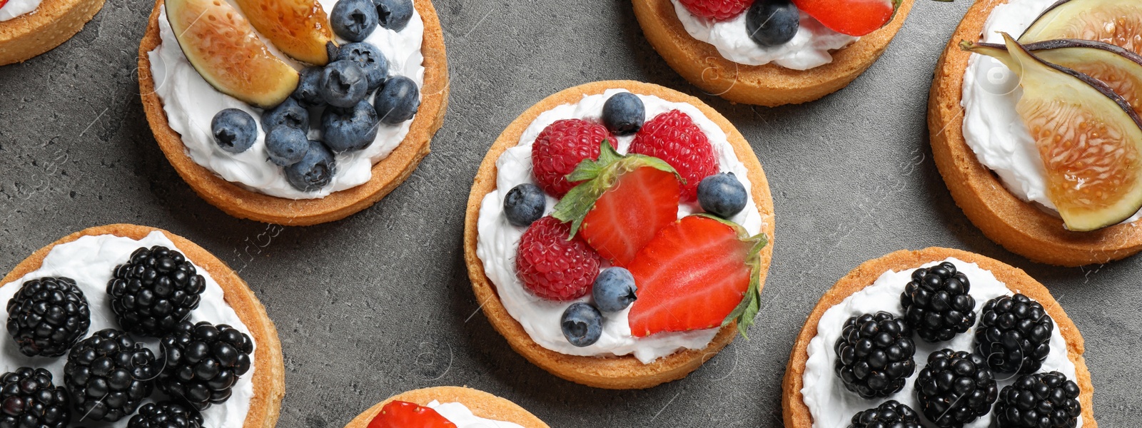 Image of Delicious tartlets with fresh berries on grey table, flat lay. Banner design