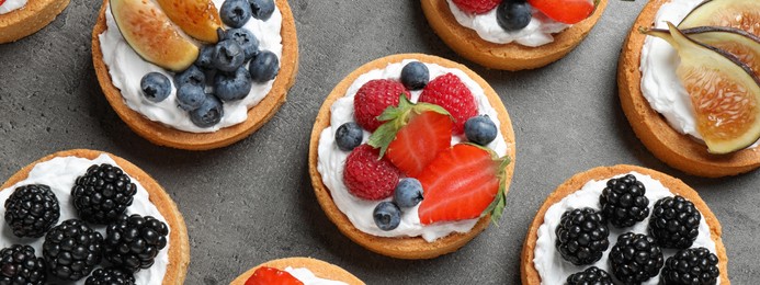 Image of Delicious tartlets with fresh berries on grey table, flat lay. Banner design