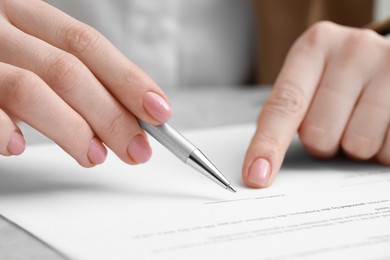Photo of Woman signing document at light grey marble table, closeup