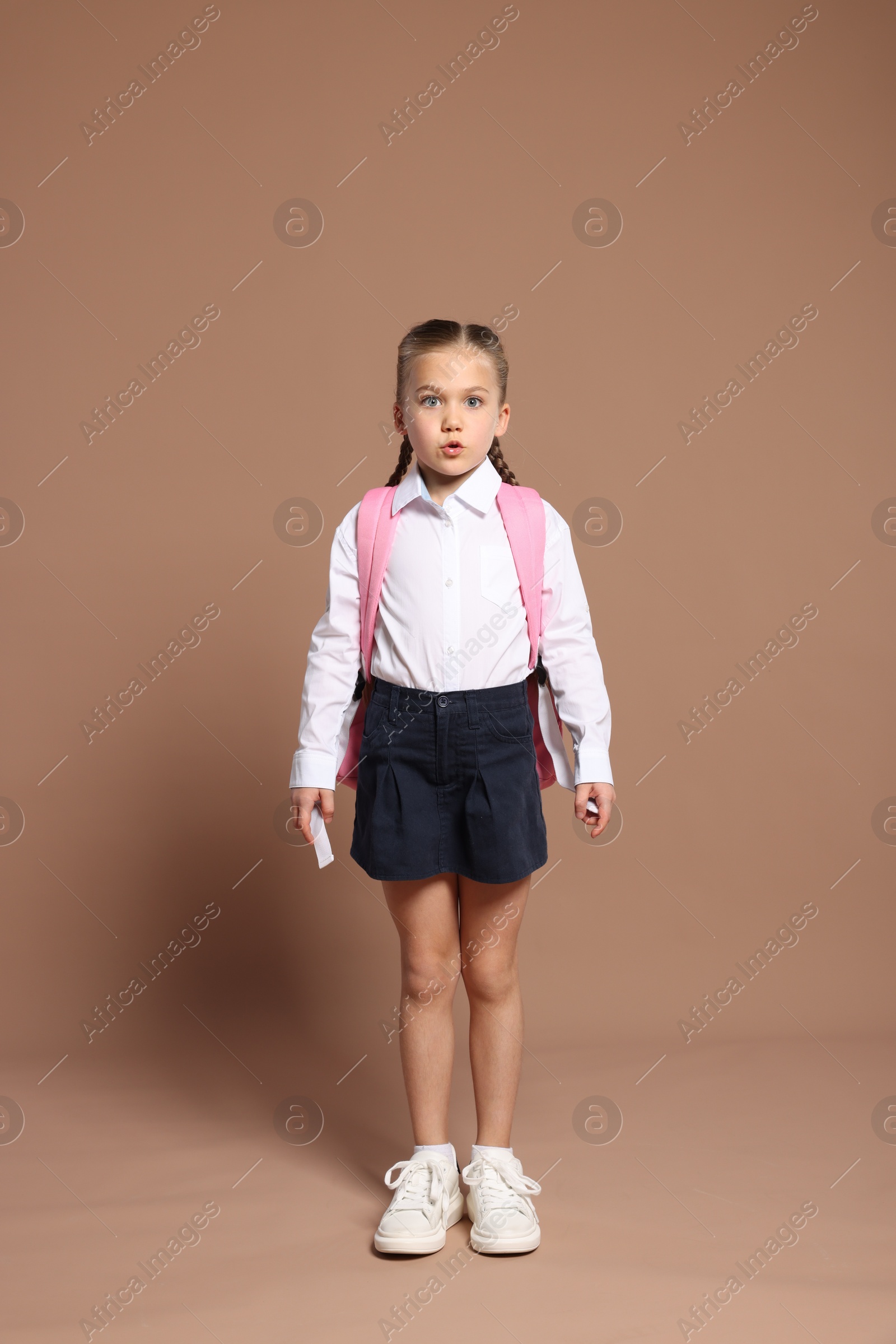 Photo of Surprised schoolgirl with backpack on brown background
