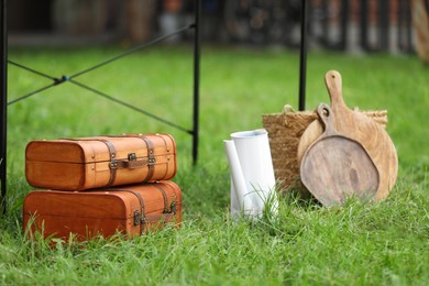 Suitcases, boards and wicker basket on green grass in yard. Garage sale