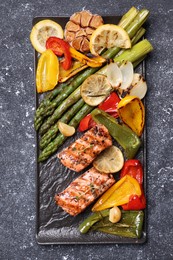 Tasty grilled salmon with lemon and vegetables on black table, top view