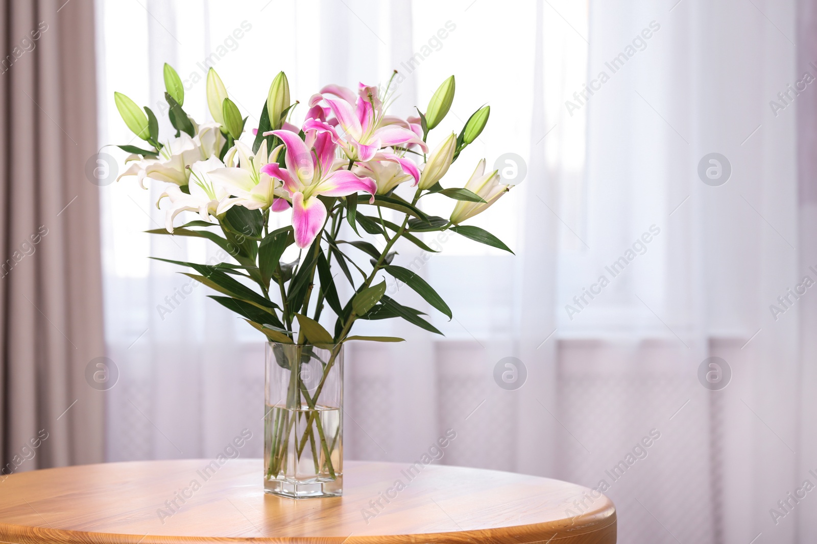 Photo of Vase with bouquet of beautiful lilies on wooden table indoors. Space for text