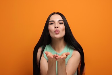 Photo of Beautiful young woman blowing kiss on orange background