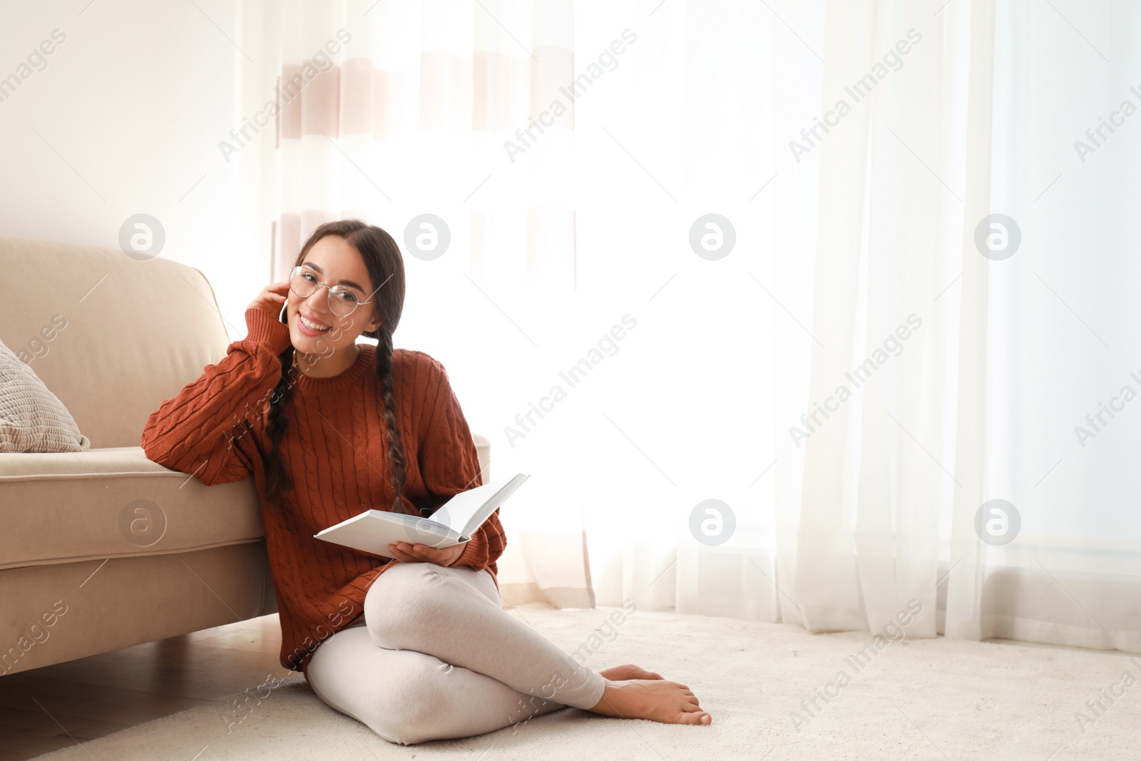 Photo of Young woman wearing knitted sweater with book at home