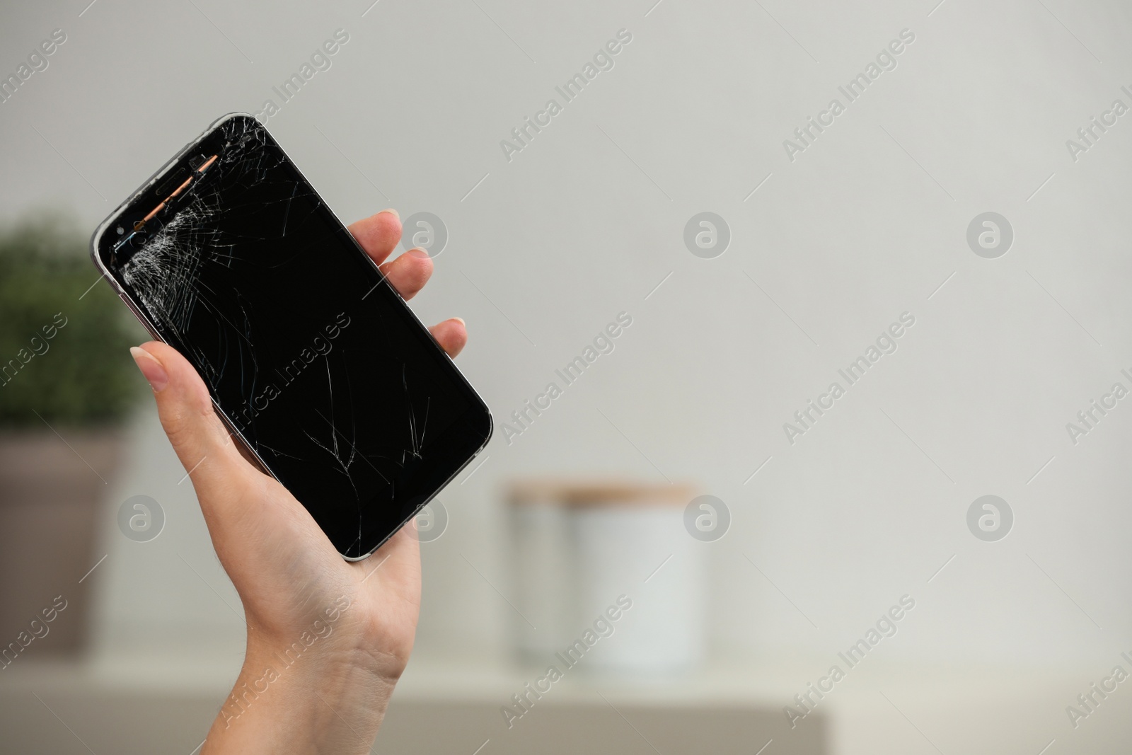 Photo of Woman holding damaged smartphone on blurred background, closeup with space for text. Device repairing