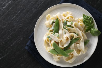 Photo of Delicious pasta with green peas and creamy sauce on black table, top view. Space for text