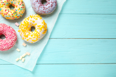 Photo of Delicious glazed donuts on blue wooden table, flat lay. Space for text