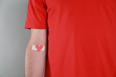 Blood donation concept. Man with adhesive plaster on arm against grey background, closeup. Space for text