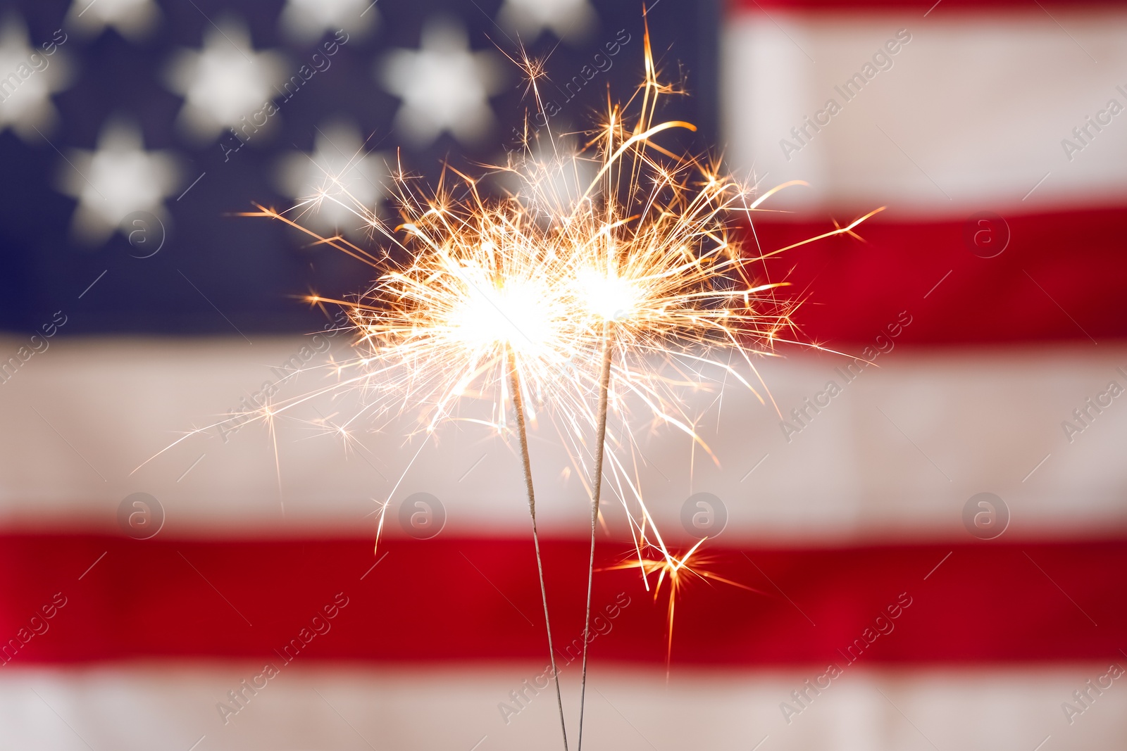 Photo of Bright burning sparklers against American flag, closeup