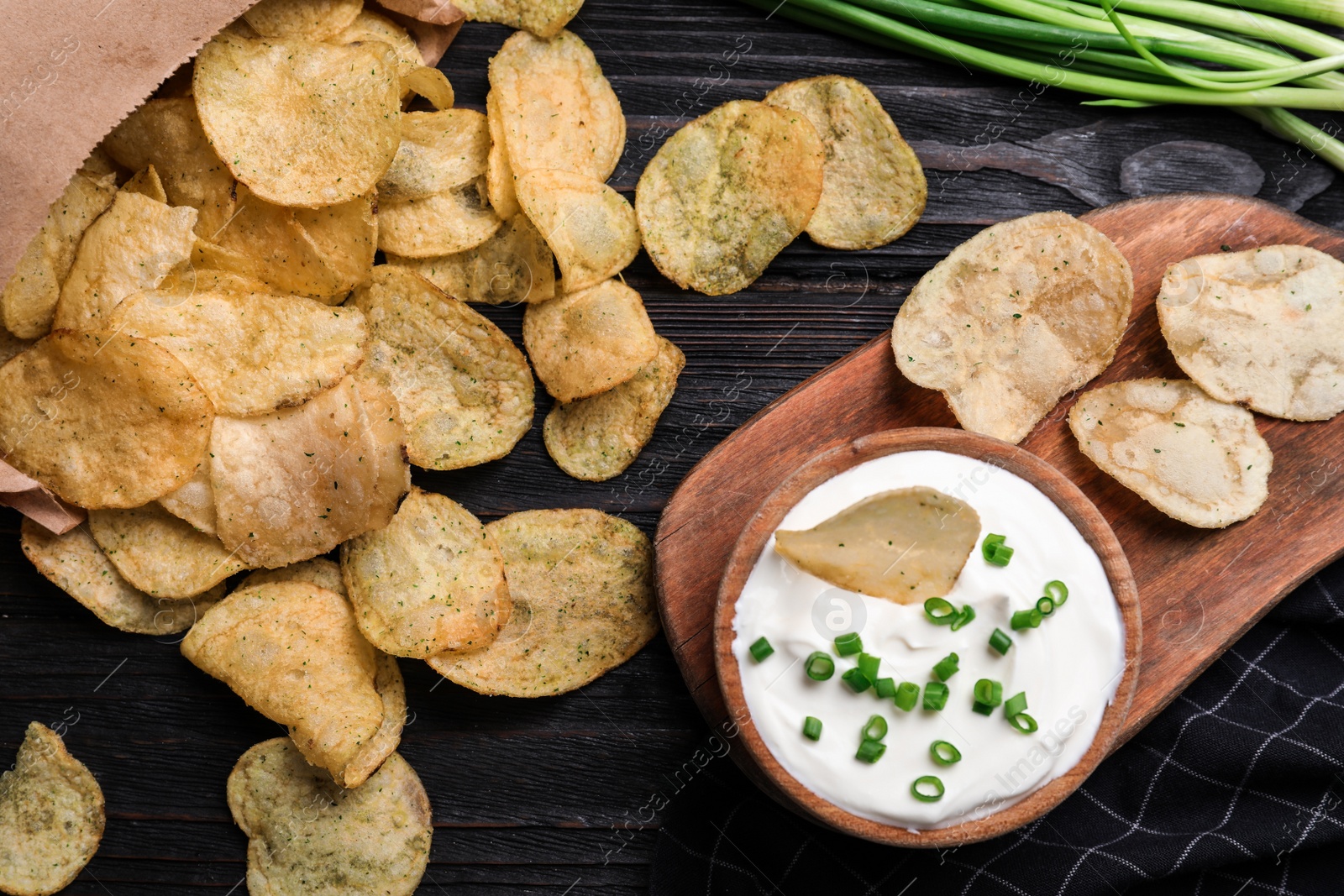 Photo of Sour cream in and chips on black wooden table, flat lay