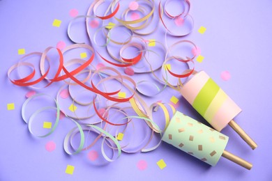 Photo of Beautiful serpentine and confetti bursting out of party poppers on violet background, flat lay