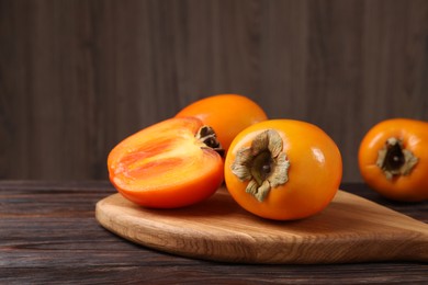 Photo of Whole and cut delicious ripe persimmons on wooden table