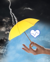Image of Insurance concept. Man covering heart illustration with yellow umbrella during storm, closeup