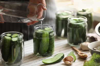 Woman pouring water into jar with canning cucumbers at table, closeup