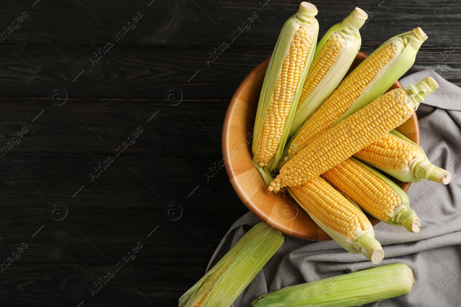 Photo of Bowl with tasty sweet corn cobs on wooden table, top view