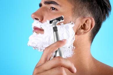 Handsome young man shaving on color background