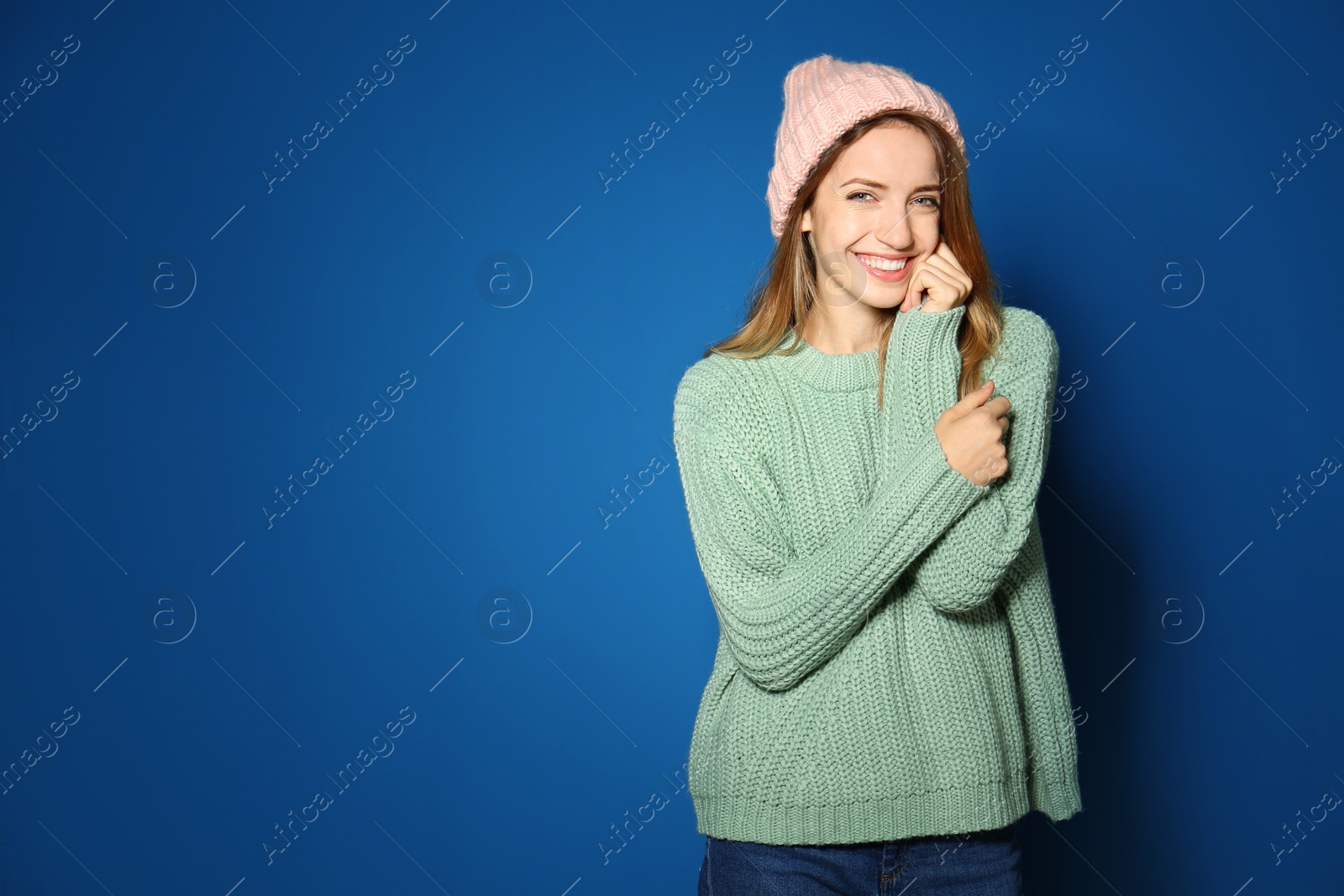 Image of Happy young woman wearing warm sweater and knitted hat on blue background. Space for text