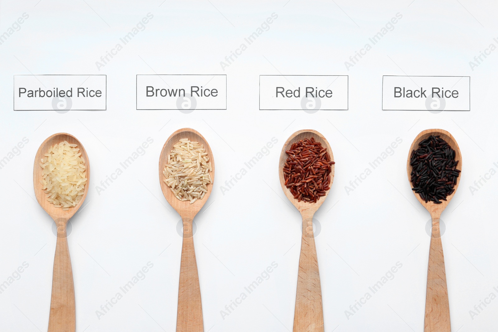 Photo of Spoons with different types of uncooked rice and cards on white background, top view