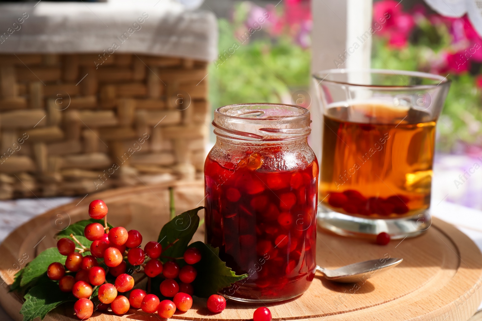 Photo of Tasty hot drink, jam and viburnum berries on wooden board indoors