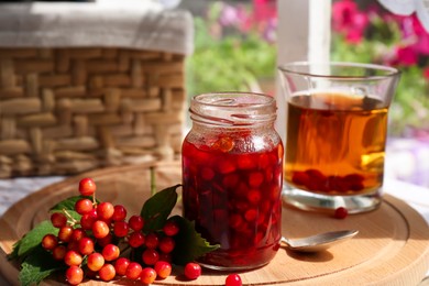 Photo of Tasty hot drink, jam and viburnum berries on wooden board indoors