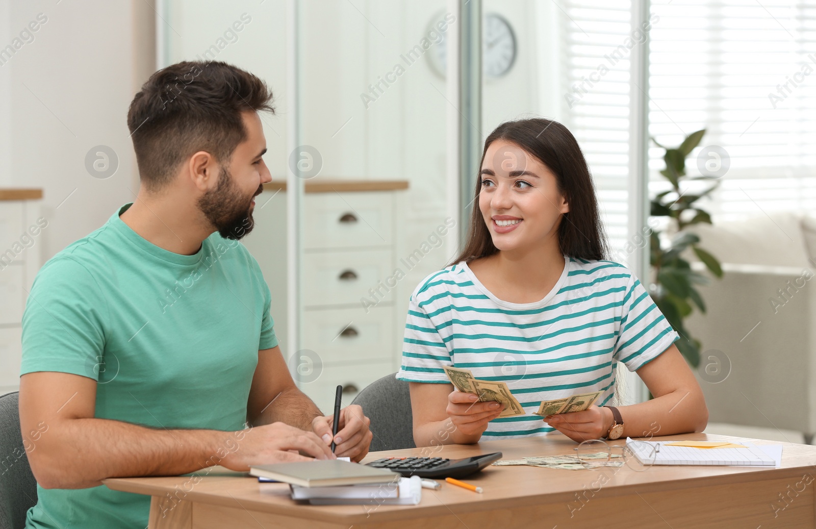 Photo of Happy young couple counting money at wooden table indoors